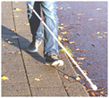 Un marcheur avec canne blanche sur un trottoir